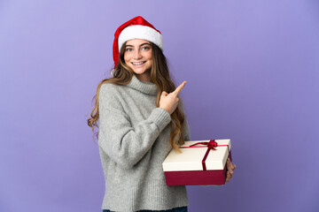 Girl with christmas hat holding a present isolated on white background pointing to the side to present a product