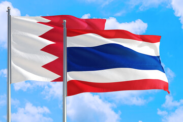 Thailand and Bahrain national flag waving in the windy deep blue sky. Diplomacy and international relations concept.