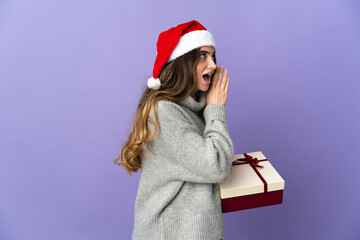 Girl with christmas hat holding a present isolated on white background shouting with mouth wide open to the side