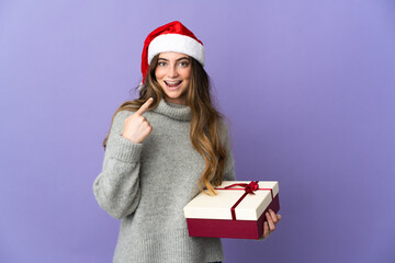 Girl with christmas hat holding a present isolated on white background giving a thumbs up gesture
