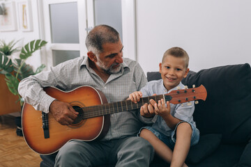 grandfather and grandson playing acoustic guitar at home
