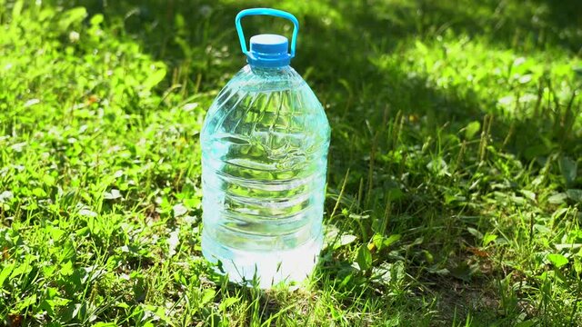 Closeup view video of big transparent plastic bottle size of 5 liters full of fresh clean water standing on grass outdoors in bright sunlight.