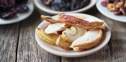 Dried apples on the foreground. Background with bowls with various dried fruits on a wooden ancient background. Home preparation of dried fruits.