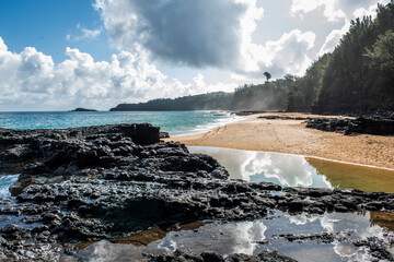 Lava rock and sand line the shore of an empty Kauai beach