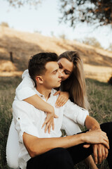 Tender girl lovingly kisses his man on the cheek while sitting on the green grass in the park.