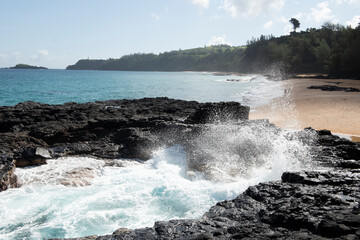 Waves crash into lava rock on empty Kauai beach