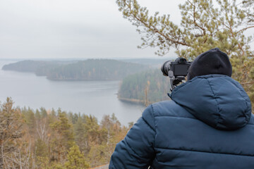 man photographing autumn landscape from the mountain
        through forests and lakes in cloudy weather and fog. rock Hiidenvuori. Finland.
