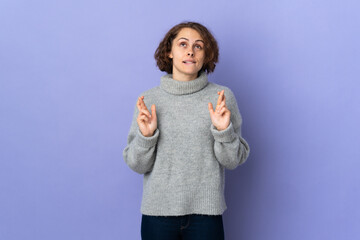 Young English woman isolated on purple background with fingers crossing and wishing the best