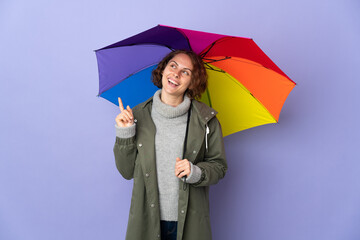 English woman holding an umbrella isolated on purple background pointing up a great idea