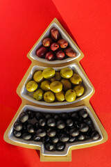 Green, black and red olives in a vase in the shape of a Christmas tree on a red background