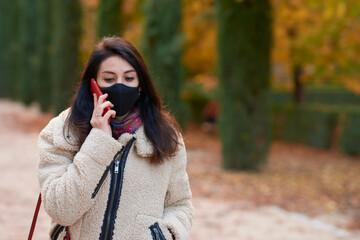 Beautiful woman with facemask calling with her smartphone in a park in autumn