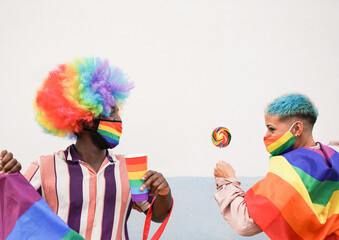 Multiracial firends dance and have fun at gay pride parade with rainbow flag while wearing...