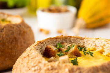 Pumpkin puree soup in a plate of bread, pumpkin soup with thyme , cheese and croutons on a white wooden background