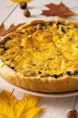 Quiche pie with mushrooms and cheese, autumn background with fallen maple and oak leaves, pine cones and hazelnuts