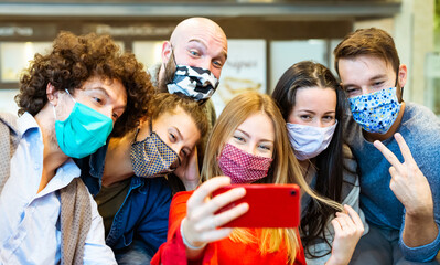 smiling group of people wearing protective face mask posing for a picture together in front of a smartphone.happy social influencers taking a selfie pic together. concept about new normal lifestyle