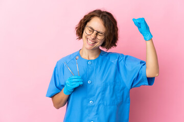 Woman English dentist holding tools over isolated on pink background celebrating a victory