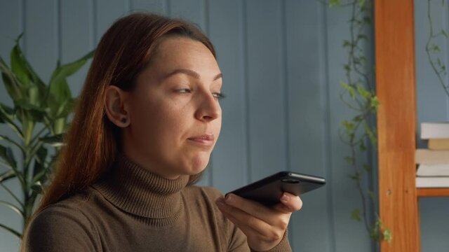 Woman sitting at workplace desk holding smartphone talking to friend on speaker phone, use phone app leave voicemail response, send voice message to colleague