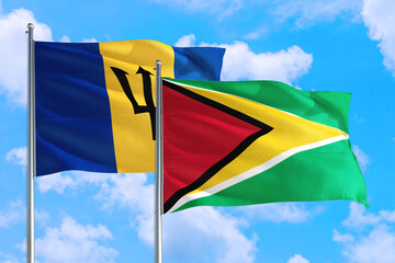 Guyana and Barbados national flag waving in the windy deep blue sky. Diplomacy and international relations concept.