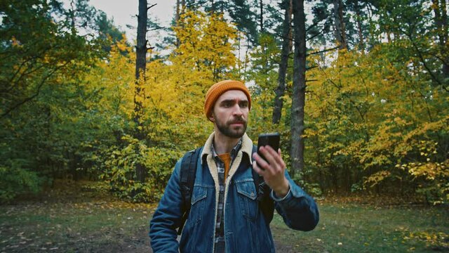 Man traveler trying to catch cell signal on phone, walking alone in autumn forest, no signal on mobile phone