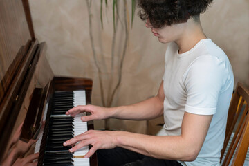 A teenager plays the piano at home, a boy learns a new piece of music, he studies remotely, online at a music school