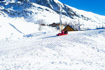 Fototapeta na wymiar Alpe D'Huez , France 30.12.2019 Two joyful kids sledding down the hills on a winter day. Blue sky