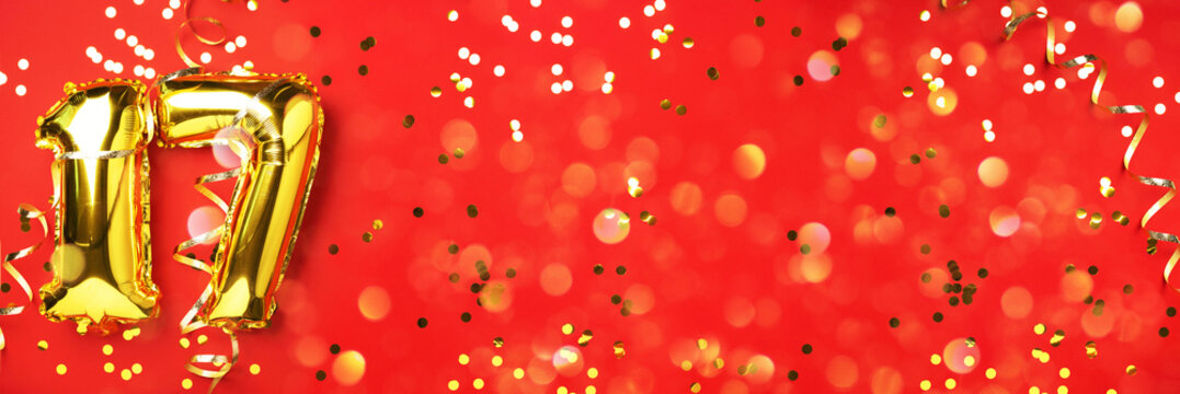 Gold foil balloon number, digit seventeen. Birthday greeting card, inscription 17. Anniversary celebration event. Banner. Stylish golden numeral, light bokeh, glitter, red background. Numerical digit