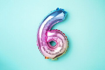 Creative layout. Rainbow foil balloon number and digit six 6. Birthday greeting card. Anniversary concept. Top view. Copy space. Stylish colored numeral over blue background. Numerical digit.