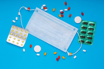 Scattered pills, ampoule blisters and syringe and a medical mask on a blue background.