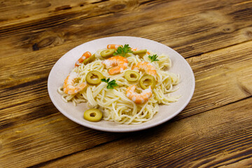 Spaghetti pasta with prawns, green olives and parsley on wooden table