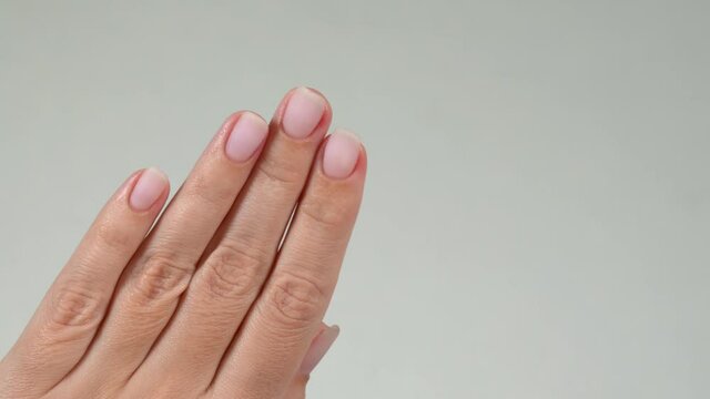 Closeup view 4k video of two manicured female hands with pastel pink trendy gel polish on beautiful short nails.