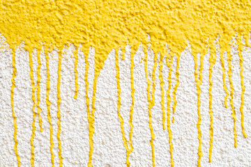 drips of yellow paint on a white wall, drops down