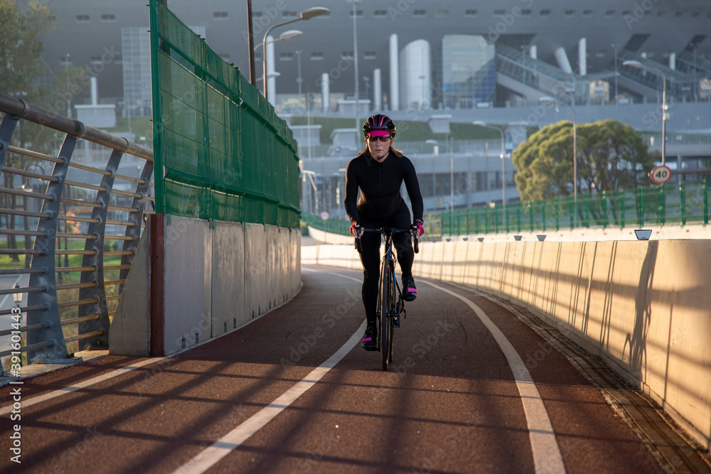 Wall mural Evening workout of a woman on a bike. Play sports in the city. Yacht Bridge St. Petersburg.