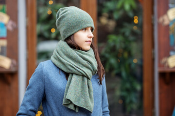 Portrait of a girl in a green hat and scarf, a walk through the Christmas city, a smile on her face, cool weather, a fascinating looking off to the side
