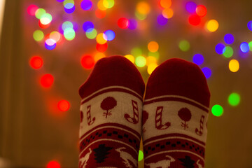 Feet In Christmas Socks In Front Of Christmas Lights. Christmas Backgrounds.
