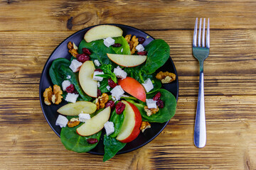 Autumn spinach salad with apple, feta cheese, walnut and dried cranberry on wooden table. Top view. Healthy vegetarian food