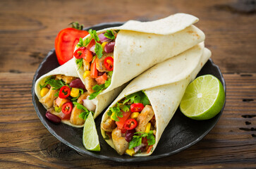 Fresh tortilla wraps with chicken meat and vegetables on the wooden table