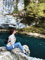 Portrait of young girl laughs while sitting on a stone near a blue lake.