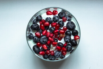 Bowl of yogurt, fresh blueberries, and seeds of pomegranate on white background. Healthy breakfast snack, top view. Fruit homemade dessert. Raw sweet vegetarian food.