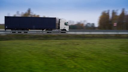 Biała ciężarówka z niebieskim kontenerem na autostradzie. Rozmyte tło