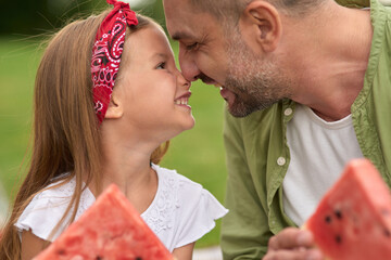 Close up of cute little girl and her loving dad touching noses while eating watermelon, family...