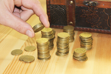 close-up of a man's hand puts coins in a stack on a wooden table against the background of a chest 