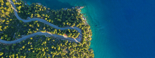 Aerial drone ultra wide top down panoramic photo of curvy snake road crossing through vegetated tropical forest by the sea