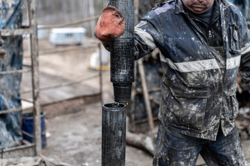 Work driller in red uniform, in helmet and goggles. He uses a hydraulic wrench to screw drill pipes...