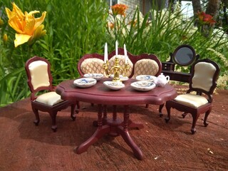 toy furniture brown sofa chairs and table with plates and candlestick on a background of a summer garden and greenery