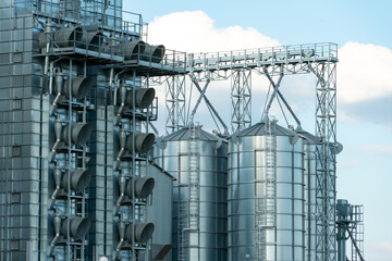 silver silos on agro manufacturing plant for processing drying cleaning and storage of agricultural products, flour, cereals and grain. Large iron barrels of grain. Granary elevator