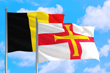 Guernsey and Belgium national flag waving in the windy deep blue sky. Diplomacy and international relations concept.