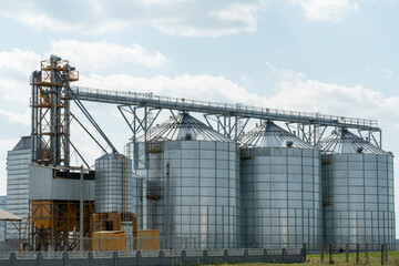 Fototapeta na wymiar silver silos on agro manufacturing plant for processing drying cleaning and storage of agricultural products, flour, cereals and grain. Large iron barrels of grain. Granary elevator