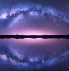 Milky Way arch reflected in water. Night landscape with bright arched milky way, purple sky with...