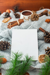 Christmas background. pine cones and green needles. plain white sheet of paper. knitted gray blanket. cup of hot cocoa. wood table.