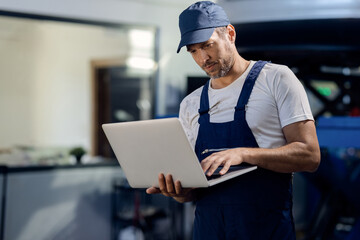Mid adult repairman using laptop at car workshop.